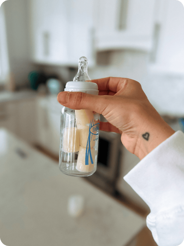 A bottle is held up in the middle of the frame, with cubes of frozen breast milk thawing inside.