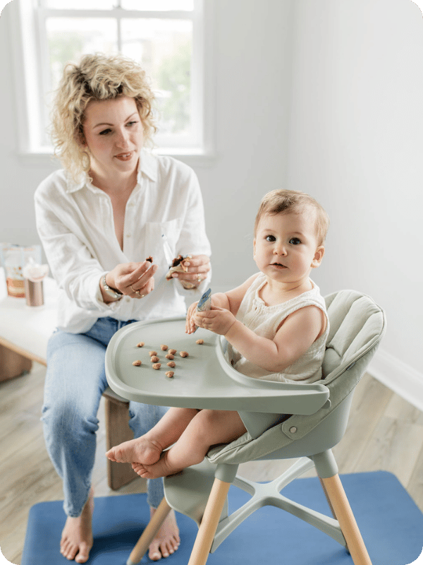 Mom gives baby peanut butter infused puffs in he high chair.