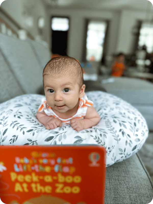 A newborn practices tummy time propped on a pillow, with a book to look at in the foreground.