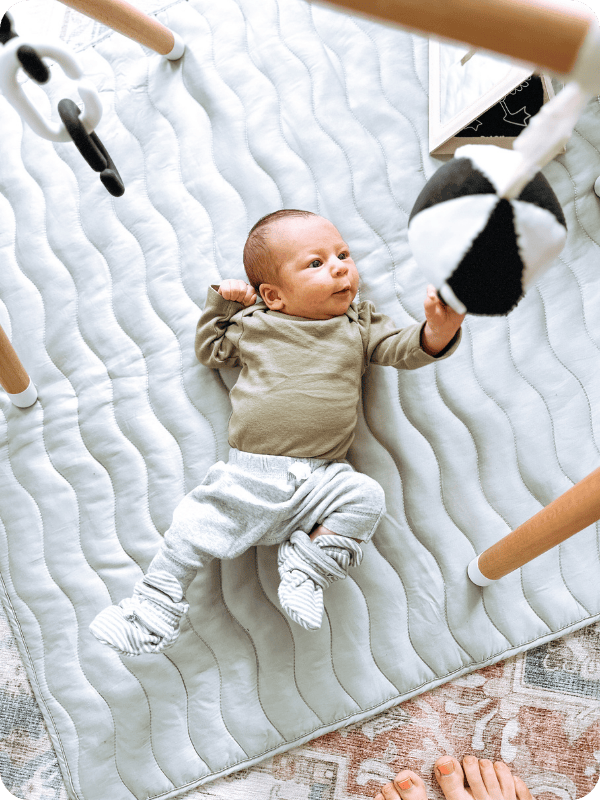 Newborn plays on the floor in a play gym