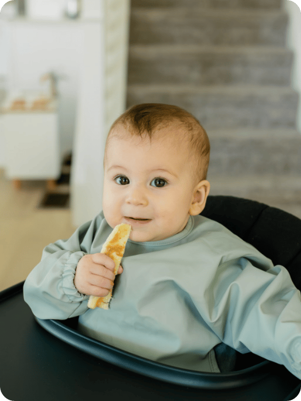 Baby in a high chair holds up a spear of banana.