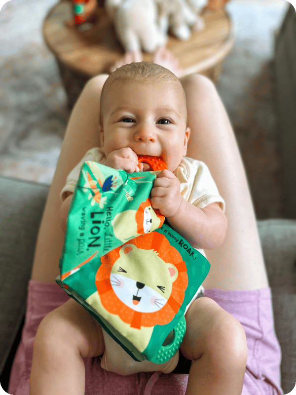 Young infant holds a crinkle book up to her mouth to explore its texture