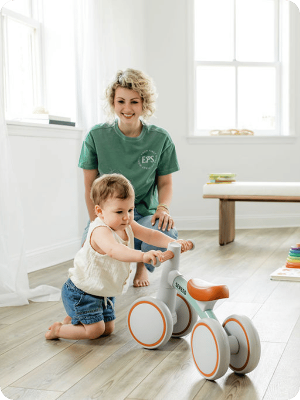 Baby kneels to reach for the handlebars on a balance bike.