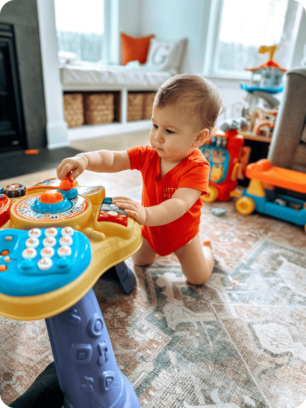9 month old kneels to play with a toy.