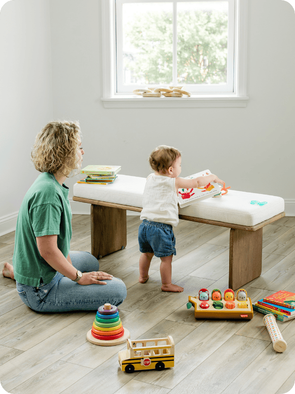 Baby stands at bench while mom watches over