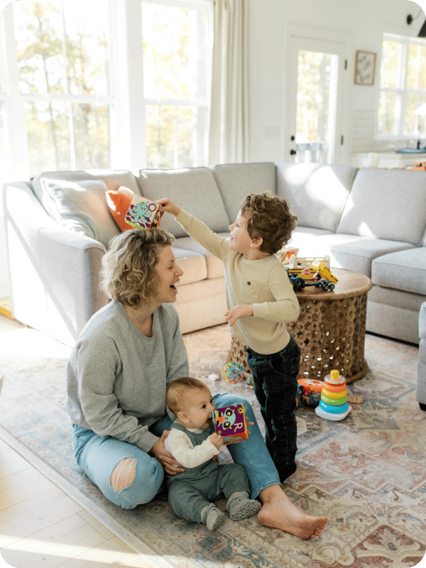 Mom and baby play with big brother on the floor.