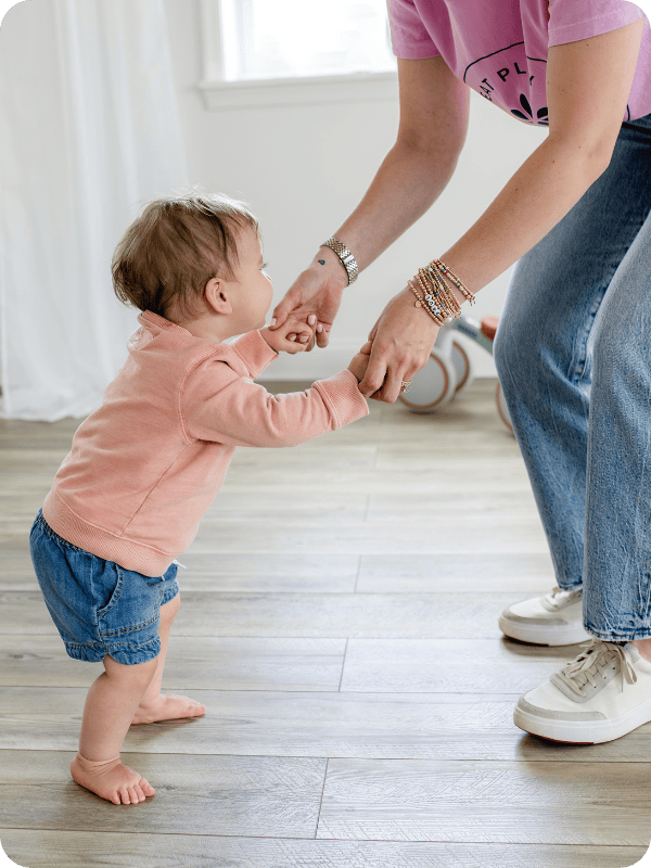 One year old holds onto mom's hands, keeping baby's arms at or below their shoulders for best support and balance.