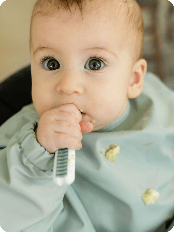 Closeup photo of baby looking at the camera while eating from a spoon.