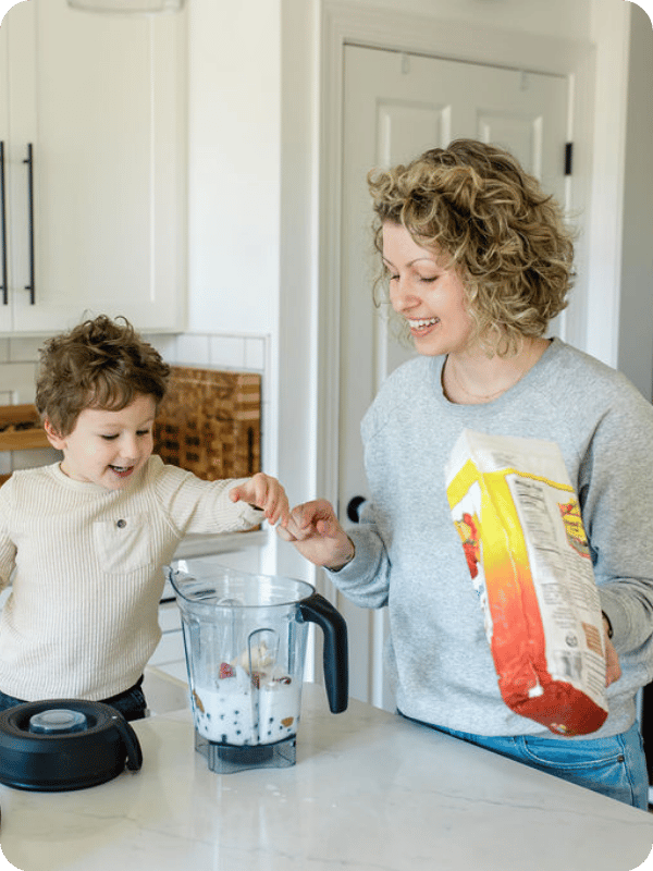 Mom and toddler make a smoothie together at the kitchen counter.