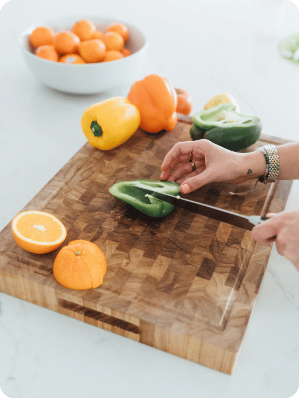 Mom cuts fresh vegetables on a butcher block cutting board.