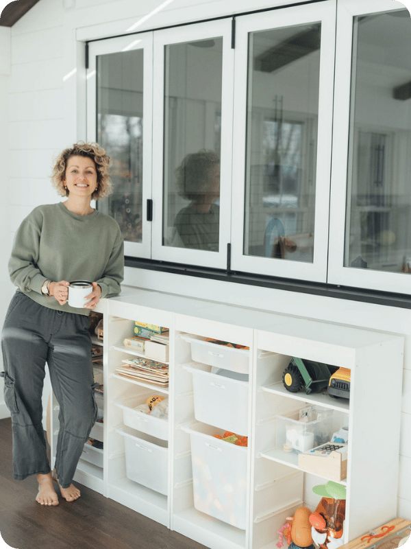 Jordyn stands beside the playroom toy organizer from Ikea with a cup of coffee in hand.