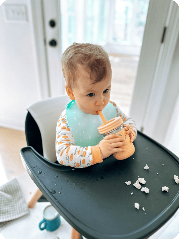 Infant drinks from straw cup while sitting in her high chair