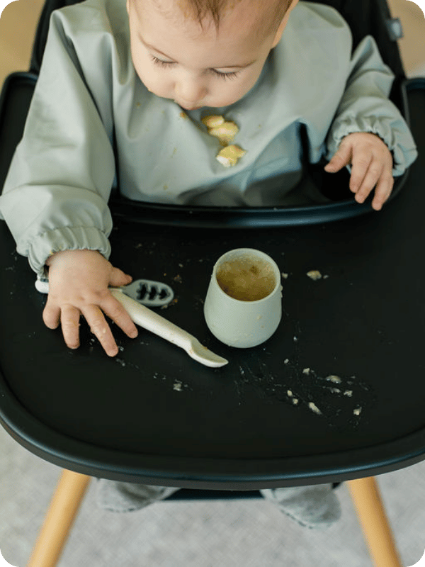 Photo looking down at baby and a cup of applesauce in the high chair.
