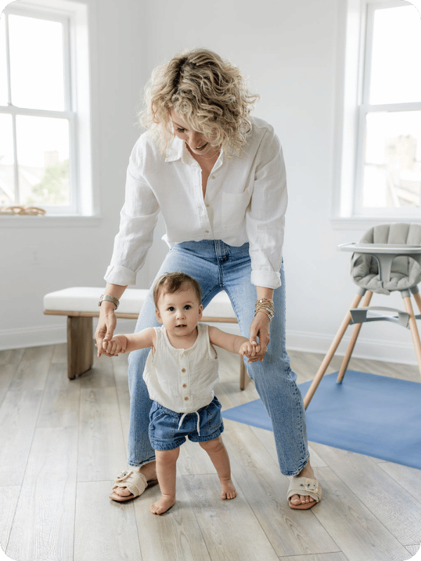 Mom holds infant's hands as she begins to walk