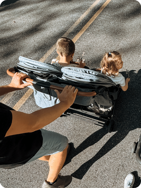 Zoe twin travel stroller being pushed with two kids on the road