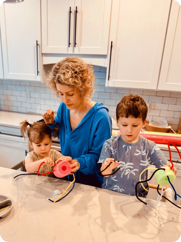 Mom and two toddlers work on a craft at the kitchen island.