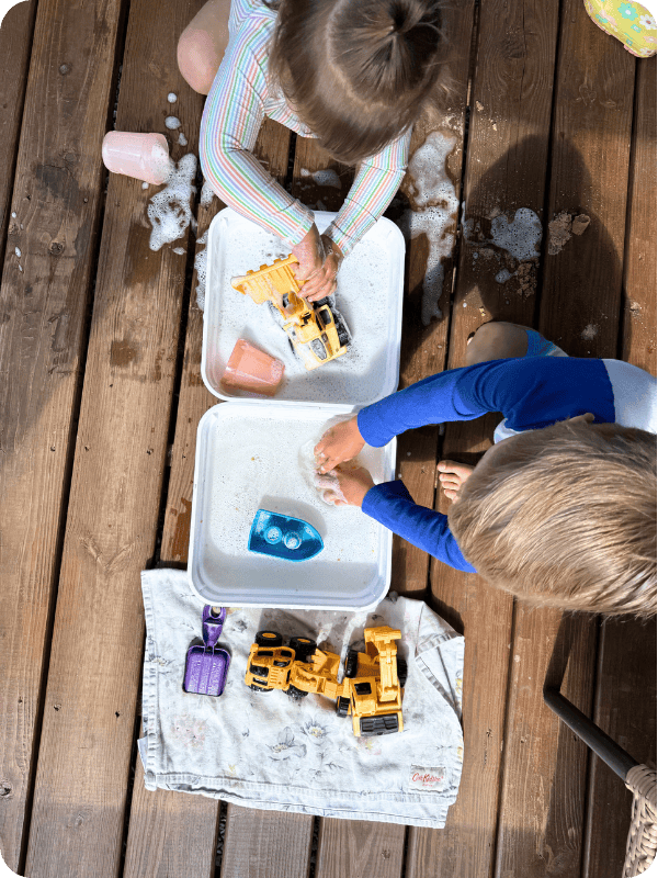 Two toddlers play at a toy washing station on the back porch.
