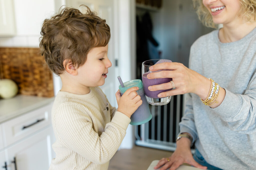 A mother and child enjoying a smoothie together in the kitchen. 