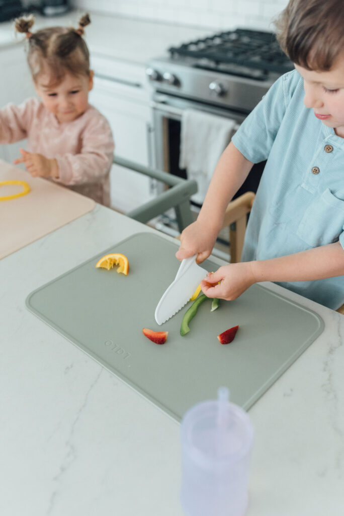 toddler boy standing in a learning tower and cutting soft fruits and veggies with toddler safe knife set