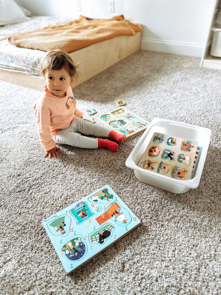 toddler girl sitting on the floor interacting with different types of puzzles