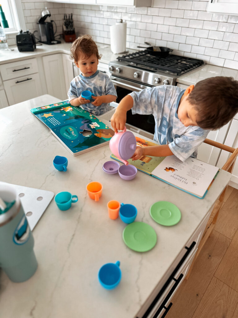 3 year old boy and 1 year old girl in two toddler towers at the counter pretending to host a tea party
