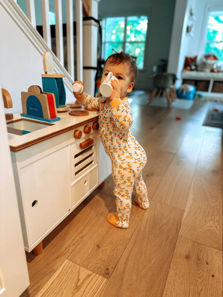 toddler drinking from a pretend coffee cup, interacting with Melissa & Doug's coffee maker at her play kitchen