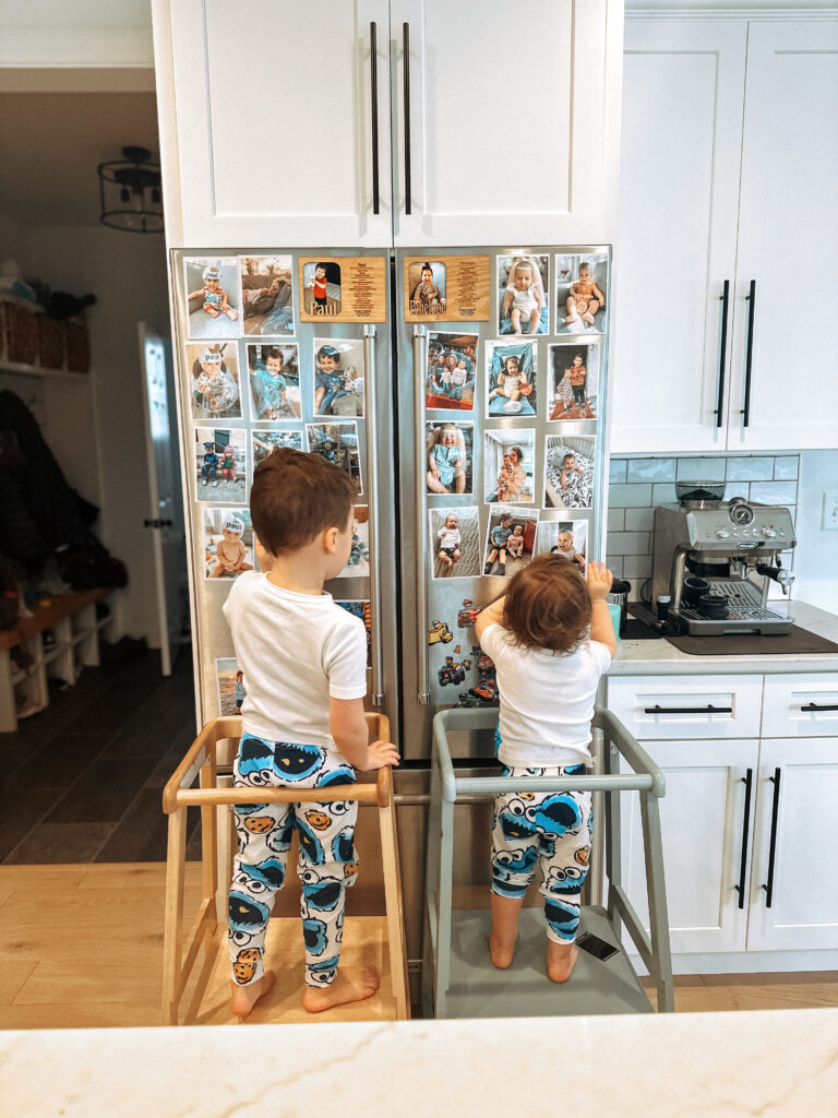 toddler boy and toddler girl both in their own learning tower looking at pictures on the fridge 