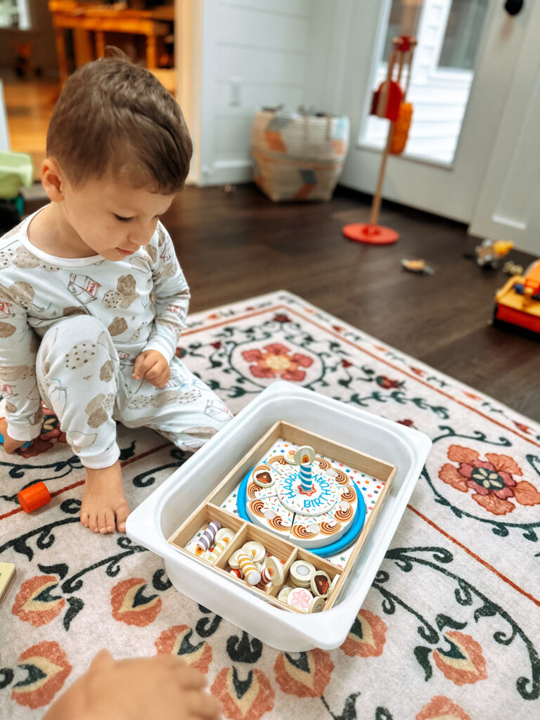 little boy looking at the toy birthday cake deciding what toppings to use during pretend play