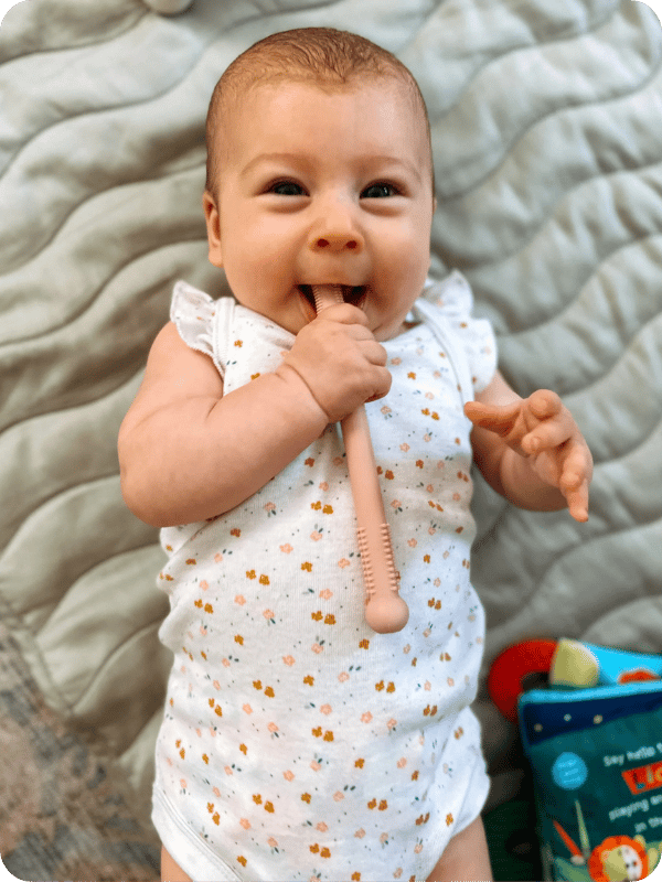 Infant smiles at the camera while playing with a hollow stick teether