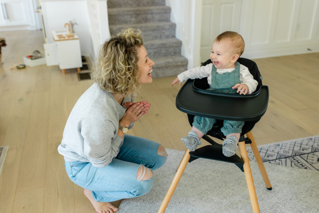 Mom laughs as baby sits in the high chair.