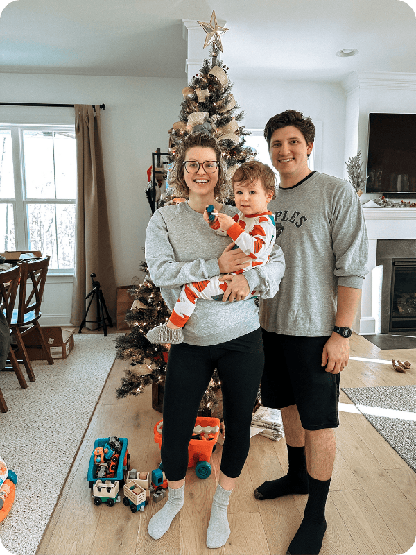 family of 3 in front of a Christmas tree with mom wearing Storq maternity leggings styled with an oversized sweatshirt
