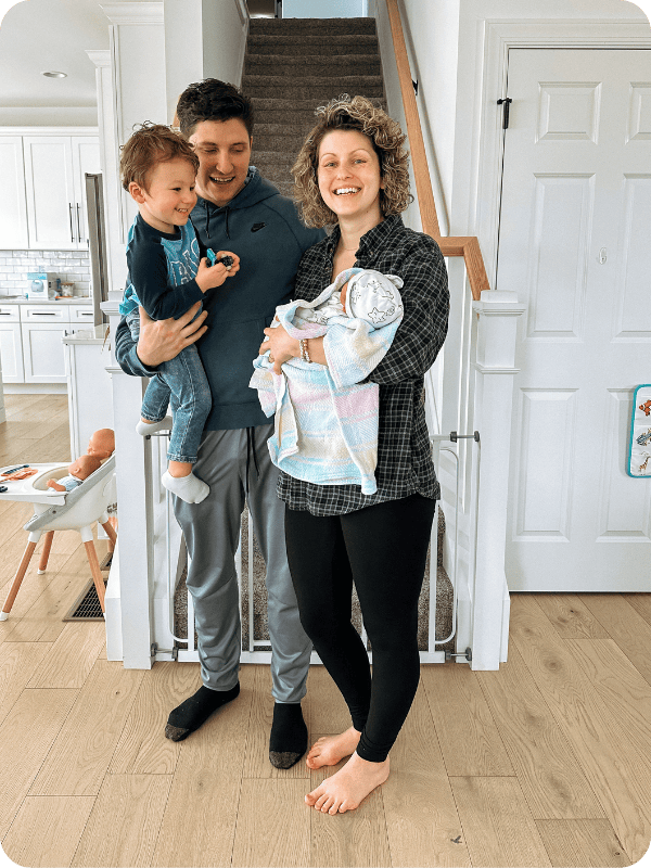 mom wearing Storq maternity leggings styled with a flannel shirt with a newborn baby in her arms - dad and brother smiling 