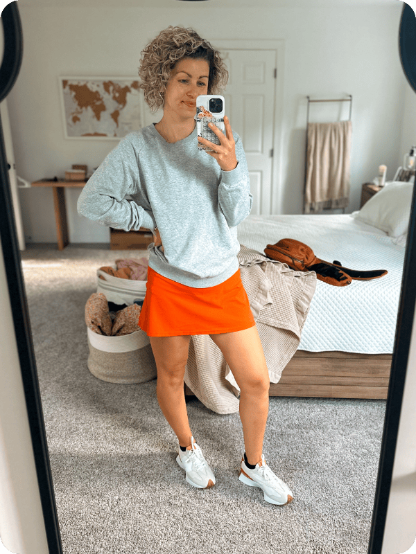 Pregnant woman wearing burnt orange maternity tennis skirt styled for fall with a gray sweatshirt