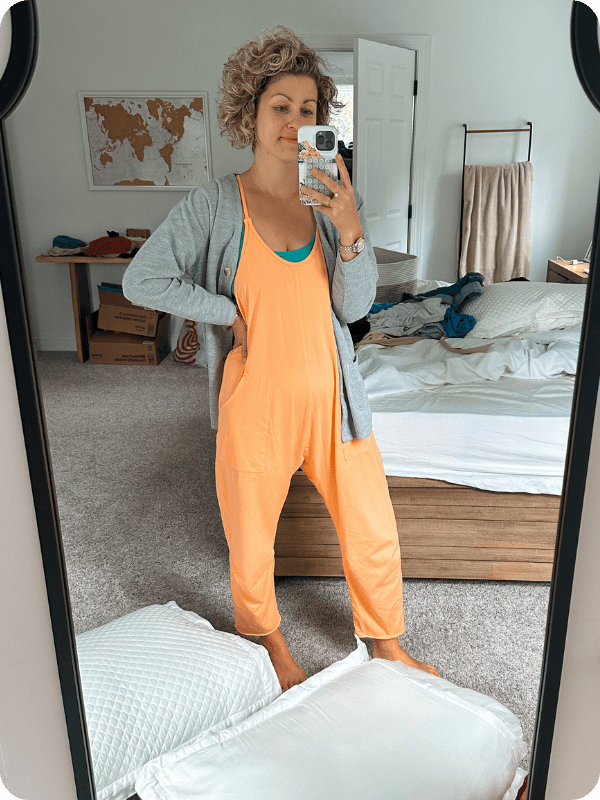 Pregnant woman wearing jumpsuit styled for fall with a cardigan