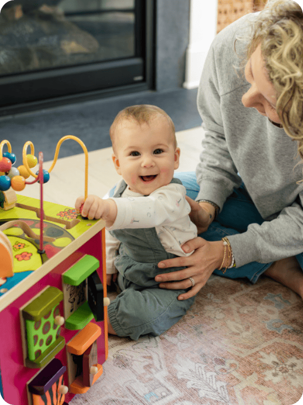 Infant sits at an activity cube with support from their mother.