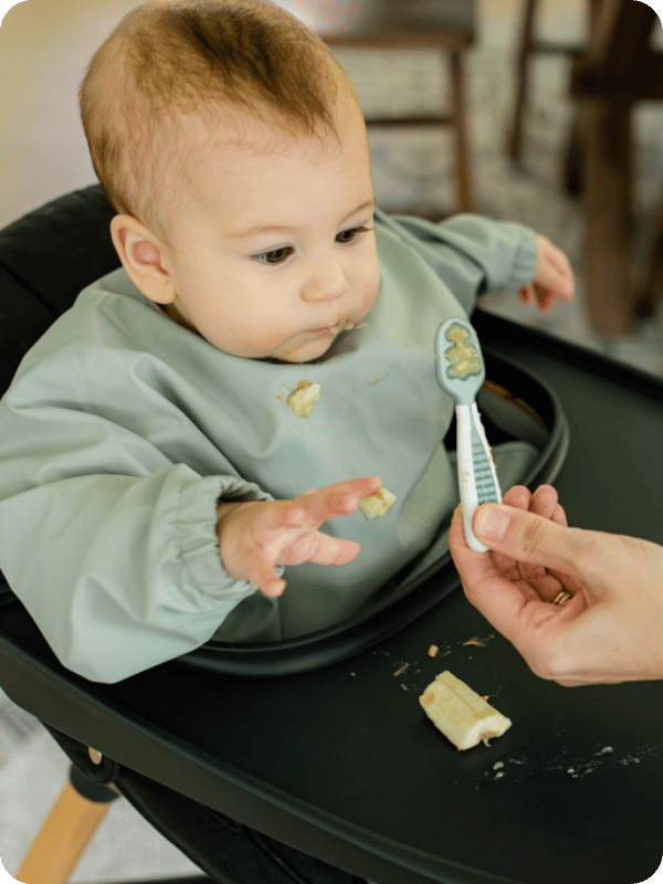 Mom offers baby a loaded spoon at meal time when starting solids.