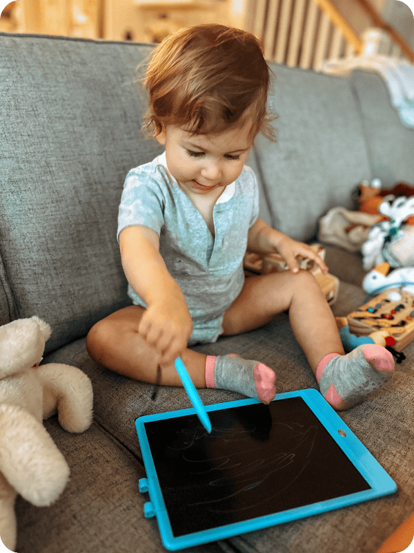 young toddler sitting on couch playing with doodle board travel toy