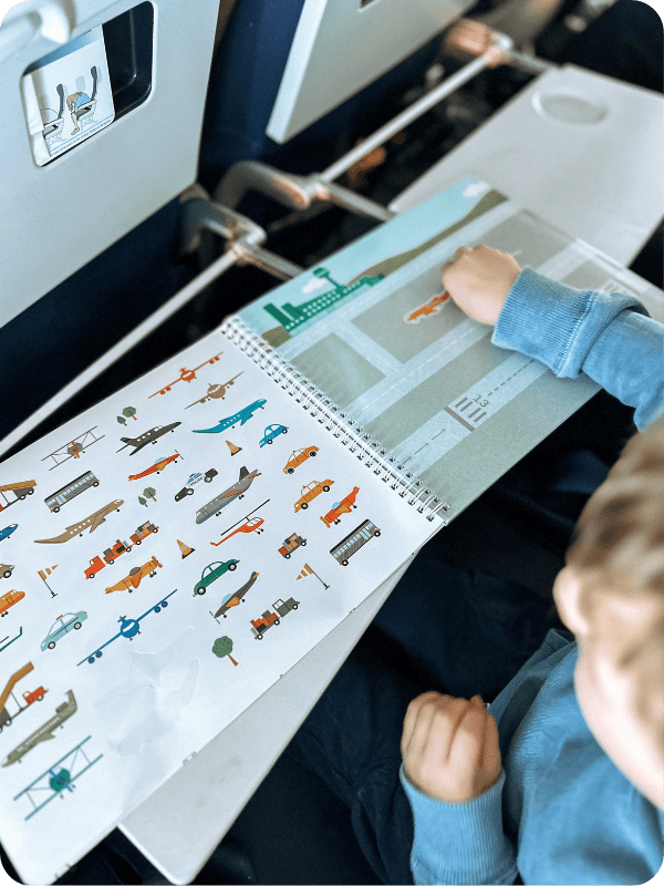 toddler playing with sticker book on plane tray table