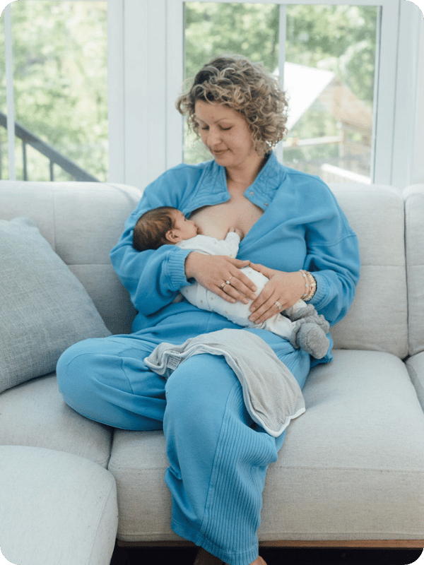 Mom sits on the couch to breastfeed her newborn.