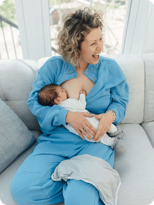 Baby breastfeeds while mom smiles at her children off camera