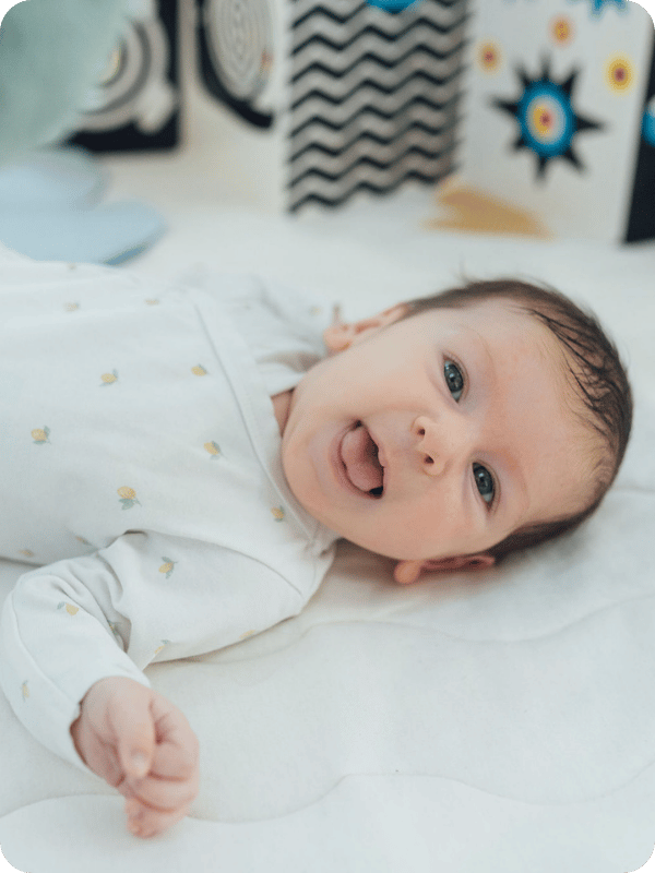 Newborn looks at the camera while laying on floor mat.