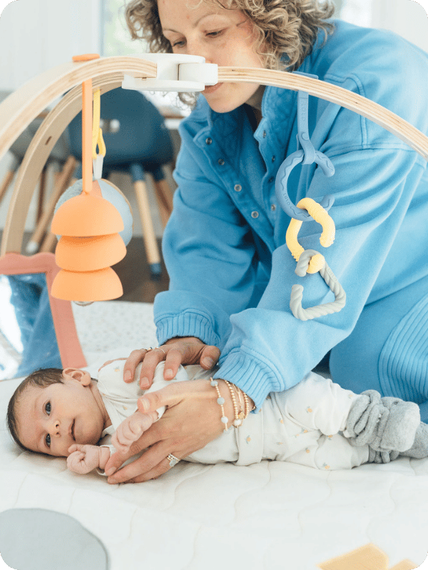 Mom helps baby get into the side lying position on her floor play gym.