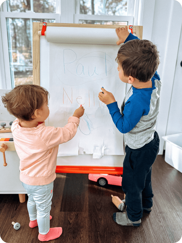 two toddlers coloring on an easel