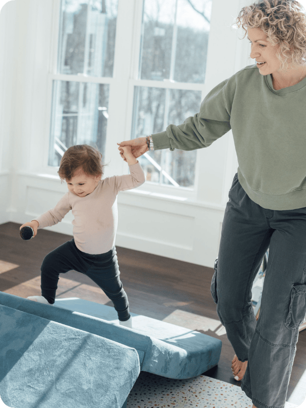 toddler walking on a play couch with parent's help