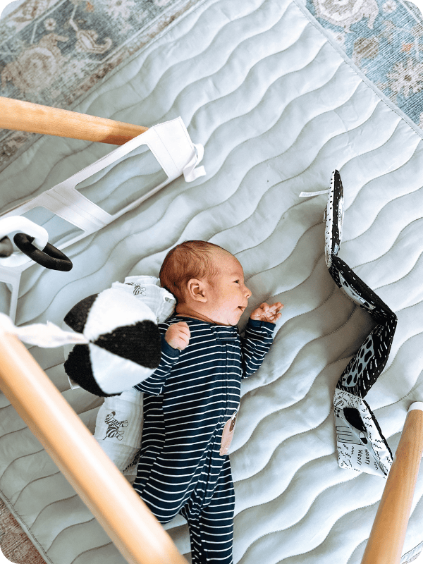 newborn baby in side-lying position looking at high-contrast toys