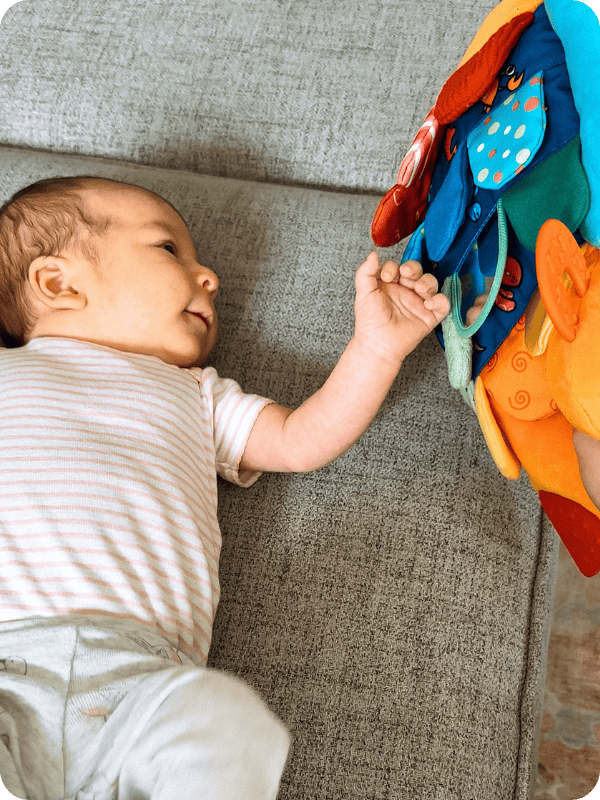 infant laying down playing with Melissa and Doug soft book