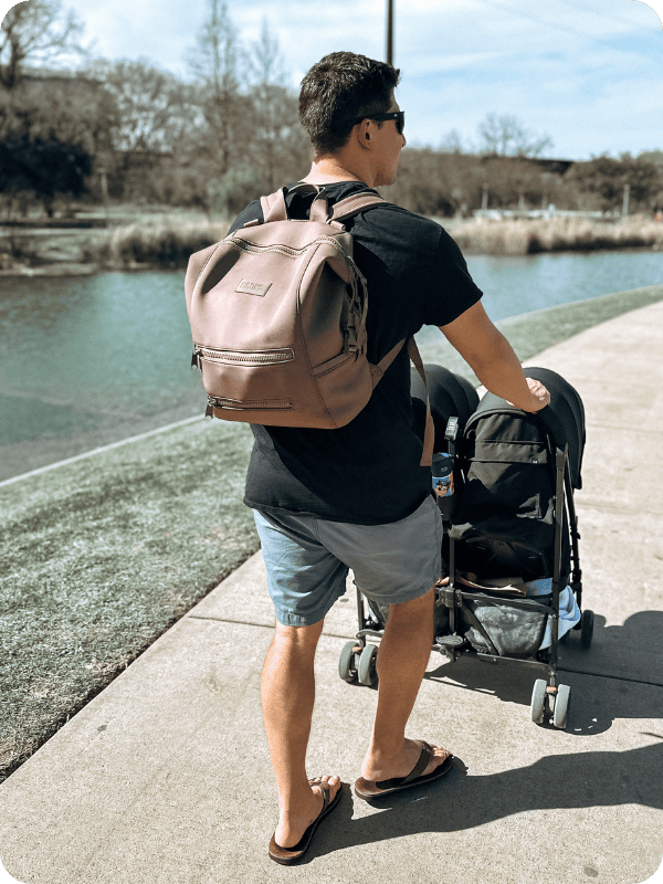 Dad pushing stroller with Dagne Dover diaper bag on his back