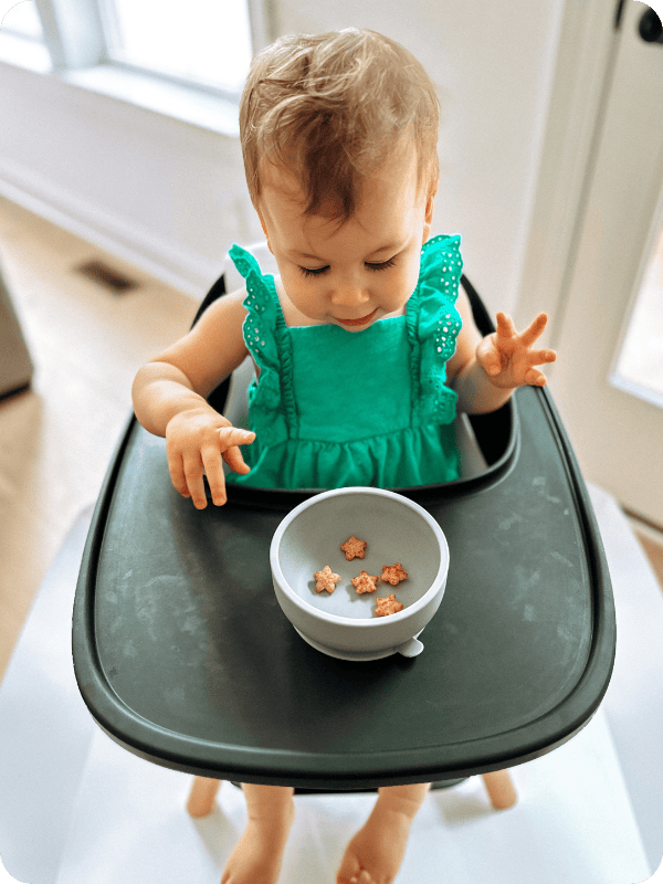 toddler eating baby puffs in a high chair