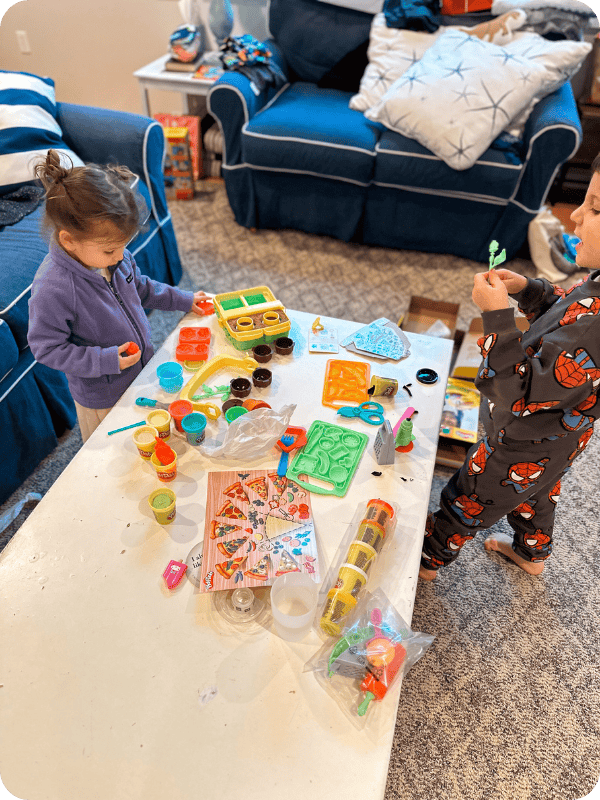 Toddlers playing with a Play Doh activity set inside.