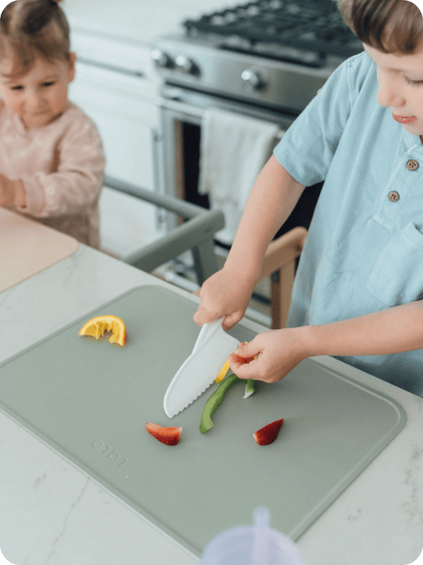 toddler using Lalo placemat to cut fruits